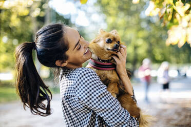 Happy young woman holding dog in a park - SODF00717