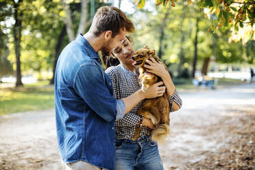 Glückliches junges Paar mit Hund in einem Park - SODF00718