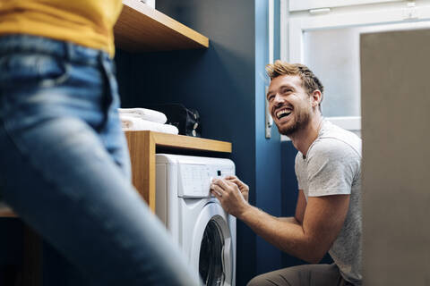 Glücklicher junger Mann, der seine Freundin ansieht und die Wäsche zu Hause wäscht, lizenzfreies Stockfoto