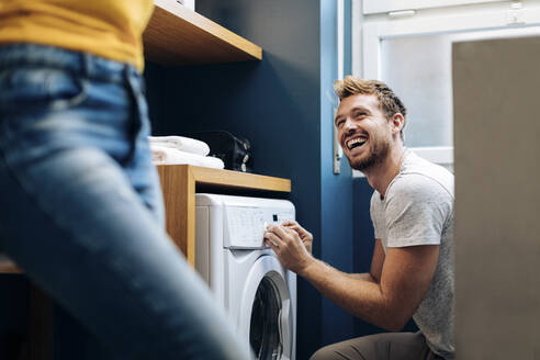 Happy young man looking at girlfriend and doing the laundry at home - SODF00726