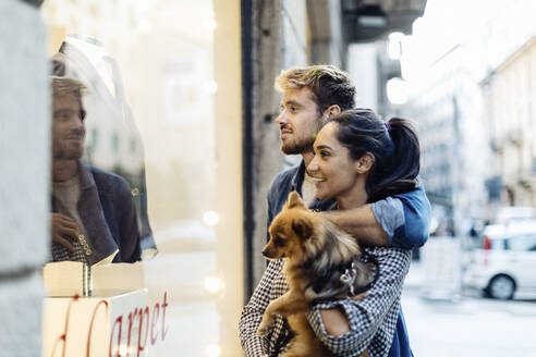 Junges Paar mit Hund schaut in ein Schaufenster in der Stadt - SODF00733