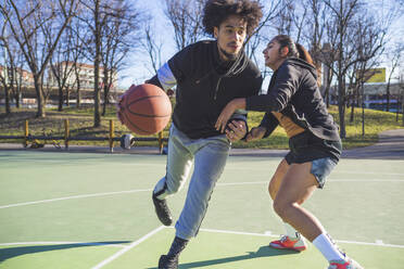 Junger Mann und Frau spielen Basketball auf dem Platz - MEUF00057