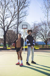 Portrait of young man and woman standing on basketball court - MEUF00059