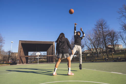 Junger Mann und Frau spielen Basketball auf dem Platz - MEUF00061