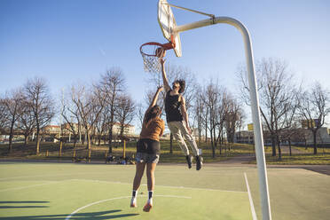 Junger Mann und Frau spielen Basketball auf dem Platz - MEUF00062