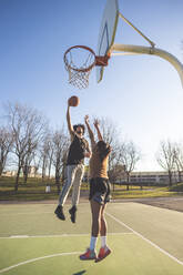 Junger Mann und Frau spielen Basketball auf dem Platz - MEUF00065