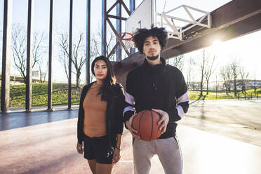 Portrait of young man and woman standing on basketball court in backlight - MEUF00071