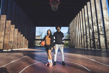 Portrait of young man and woman standing on basketball court - MEUF00072