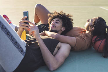 Sportliches junges Paar, das auf dem Basketballplatz liegend eine Pause einlegt - MEUF00091