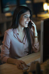 Lachende junge Frau am Telefon bei der Arbeit am Schreibtisch im Büro - JSRF00920