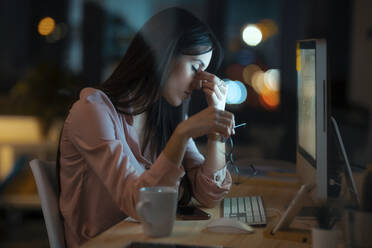 Tired young woman with eyes closed sitting at desk in office - JSRF00930