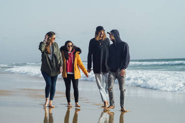 Freunde unterhalten sich in voller Länge beim Spaziergang am Strand gegen den Himmel in Tarifa, Spanien - OCMF01067