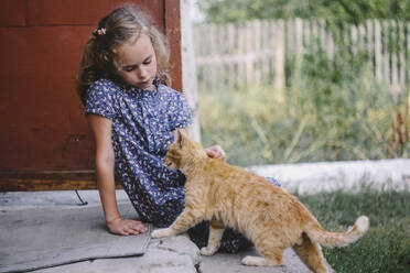 Mädchen sitzt auf einer Treppe im Freien und streichelt eine getigerte Katze - OGF00261