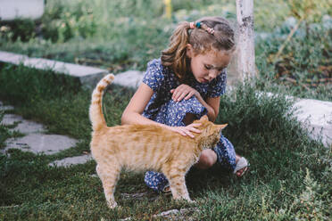 Mädchen hockt auf einer Wiese und streichelt eine getigerte Katze - OGF00262