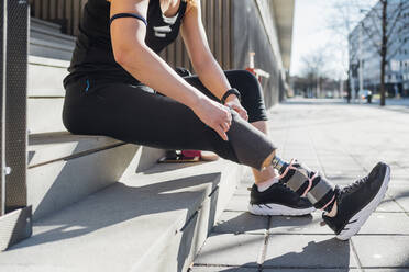 Sportliche junge Frau mit Beinprothese auf einer Treppe in der Stadt sitzend - MEUF00115