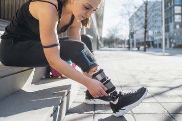 Sporty young woman with leg prosthesis sitting on stairs in the city - MEUF00116