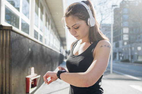 Sportliche junge Frau mit Smartwatch in der Stadt - MEUF00119