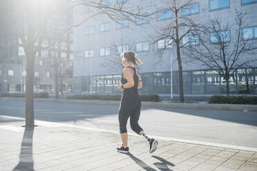 Sportliche junge Frau mit Beinprothese beim Laufen in der Stadt - MEUF00120