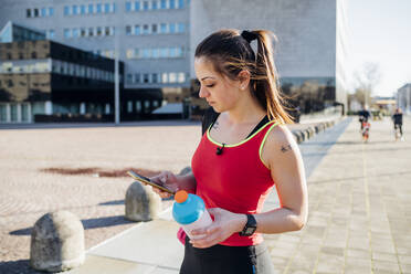 Sportliche junge Frau mit Smartphone in der Stadt - MEUF00139