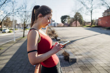 Sportliche junge Frau mit Smartphone in der Stadt - MEUF00141