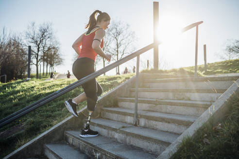 Sportliche junge Frau mit Beinprothese beim Treppensteigen - MEUF00144