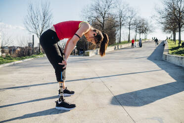 Erschöpfte sportliche junge Frau mit Beinprothese auf einem Gehweg stehend - MEUF00150