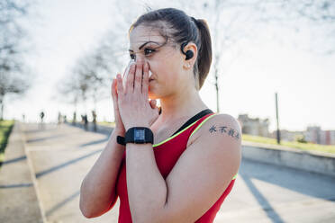 Sportliche junge Frau mit drahtlosen Kopfhörern, die sich die Nase putzt - MEUF00159