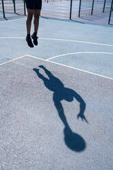 Schatten eines Mannes, der auf einem Basketballplatz Basketball spielt und einlocht - JPIF00506