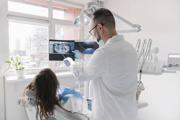 Young woman getting dental treatment in clinic, doctor explaining x-ray - AHSF02021