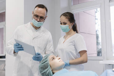 Young woman getting dental treatment in clinic, denist and assistant using digital tablet - AHSF02047