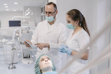 Young woman getting dental treatment in clinic, denist and assistant using digital tablet - AHSF02087