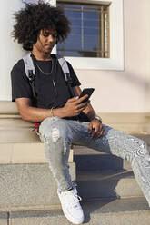 Young man listening to music and looking at his smartphone, sitting on steps - VEGF01766