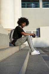 Young man listening to music and holding his smartphone, sitting on steps - VEGF01769