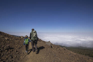 Rückansicht eines Vaters mit seinem Sohn beim Trekking in der Gegend von Arenas Negras, Teide-Nationalpark, Teneriffa - IHF00290