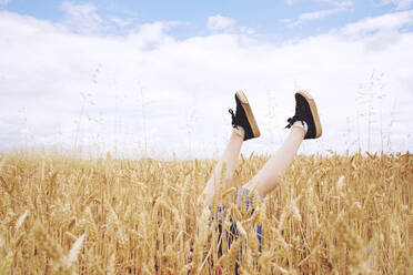 Niedriger Ausschnitt einer Frau mit hochgelegten Beinen inmitten von Getreidepflanzen auf einem Feld - EYF01188