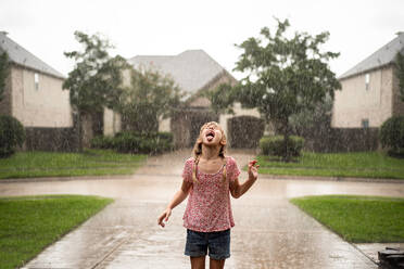 Playful Girl With Mouth Open Standing On Driveway During Rainfall - EYF01190