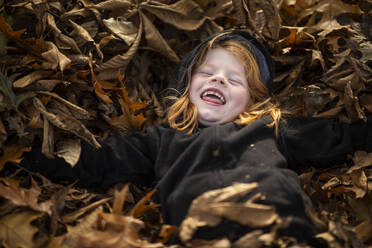 High Angle View Of Cheerful Girl Lying On Fallen Autumn Leaves - EYF01224