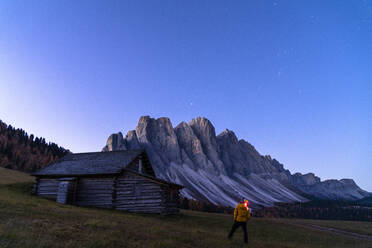 Mann bewundert die Sterne über der Geisel von der Holzhütte auf der Gampen Alm, Funes Tal, Dolomiten, Provinz Bozen, Südtirol, Italien, Europa - RHPLF14199