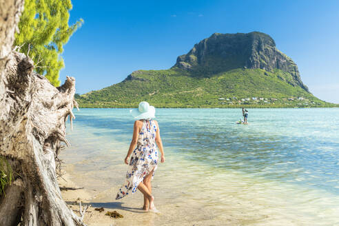 Frau am tropischen Strand mit Blick auf Paddleboard in der Lagune, La Gaulette, Le Morne Brabant, Black River, Mauritius, Indischer Ozean, Afrika - RHPLF14202