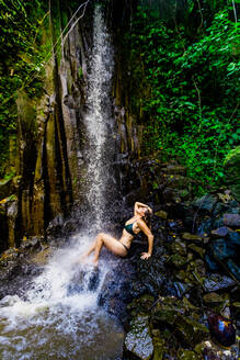 Frau posiert für ein Foto unter einem Wasserfall im Beji Guwang Hidden Canyon, Bali, Indonesien, Südostasien, Asien - RHPLF14230
