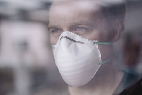 Portrait of man wearing protective mask behind windowpane - JOSEF00108