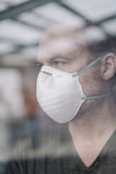 Portrait of man wearing protective mask behind windowpane - JOSEF00109