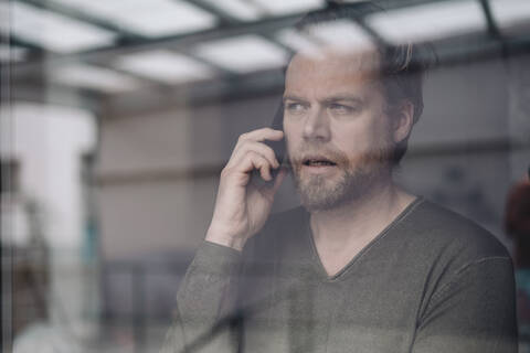 Porträt eines telefonierenden Geschäftsmannes hinter einer Fensterscheibe, lizenzfreies Stockfoto