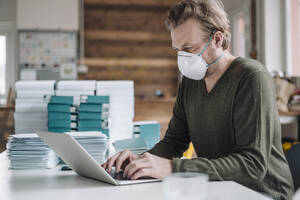 Businessman wearing protective mask and using laptop - JOSEF00115