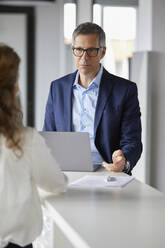 Businessman with laptop looking at businesswoman in office - RBF07165