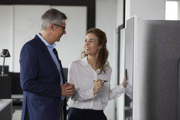 Smiling businesswoman and businessman working together at a board in office - RBF07168