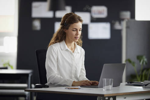 Businesswoman with headset and laptop working at desk in office - RBF07176