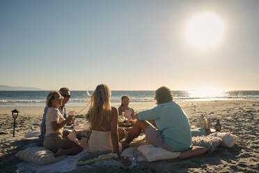 Ältere männliche und weibliche Freunde mit Mädchen genießen das Abendessen am Strand Picknick gegen den Himmel bei Sonnenuntergang. Riviera Nayarit, Mexiko - ABAF02290