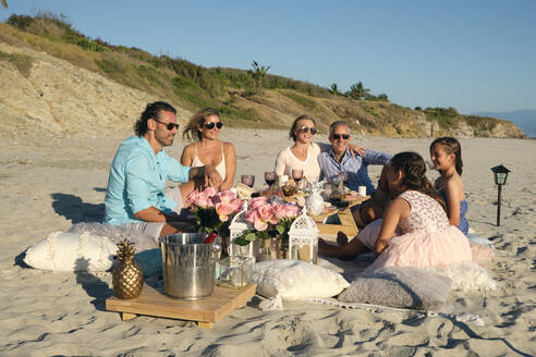 Family and friends enjoying picnic while sitting at beach against blue sky during sunset. Riviera Nayarit, Mexico - ABAF02292