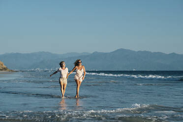 Unbeschwerter Spaziergang reifer Lesben am Strand gegen den klaren blauen Himmel, Riviera Nayarit, Mexiko, in voller Länge - ABAF02299